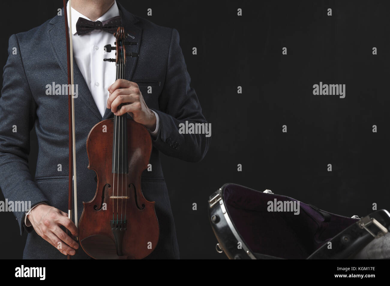 Portrait de man holding violin debout par cas sur fond noir Banque D'Images