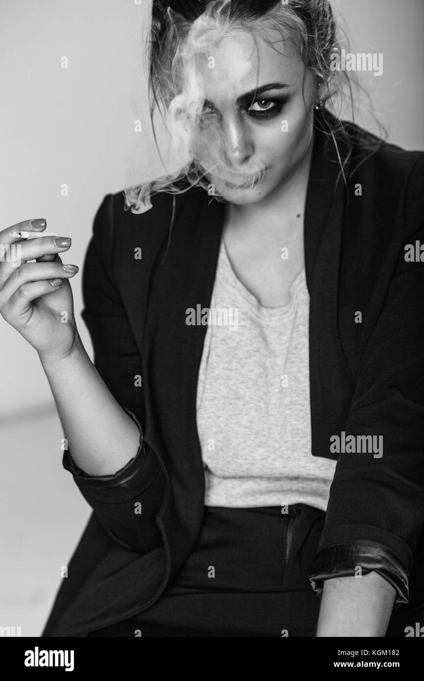 Portrait de jeune femme cigarette alors qu'il était assis à l'arrière-plan gris Banque D'Images