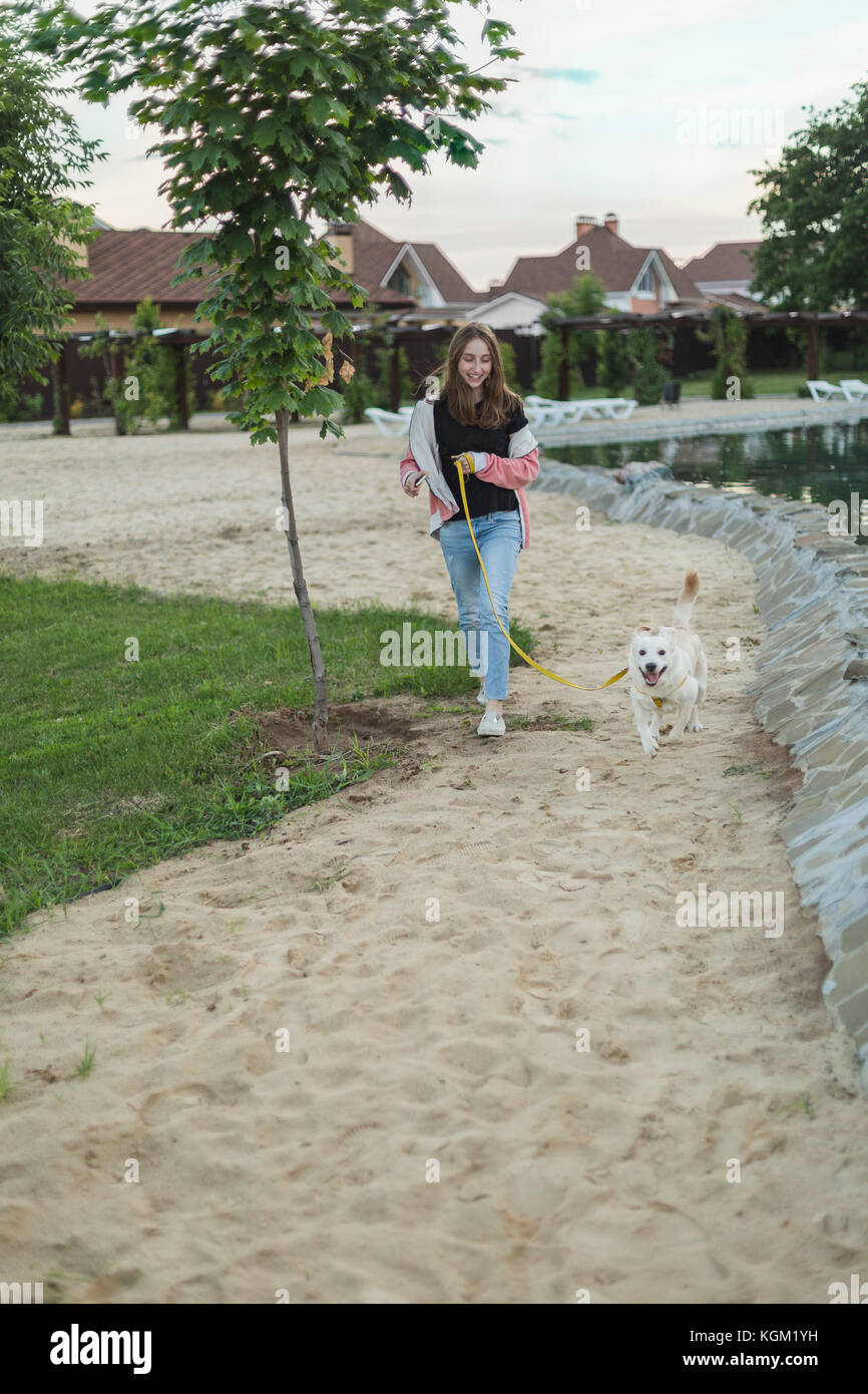 Smiling teenage girl walking with dog on sand Banque D'Images