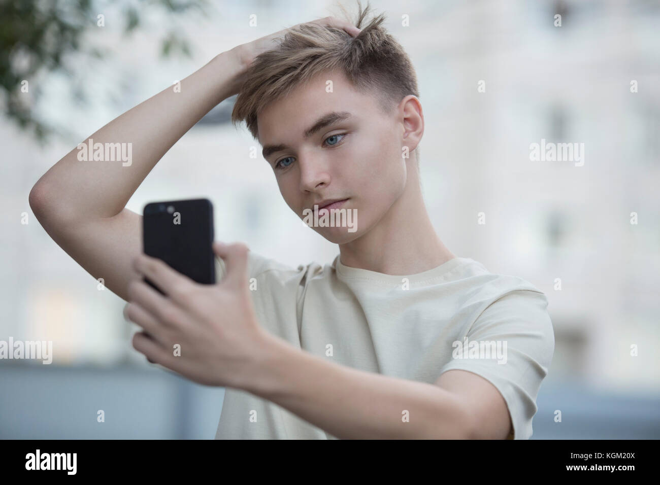 Teenage boy en tenant des selfies téléphone mobile avec la main dans les cheveux Banque D'Images