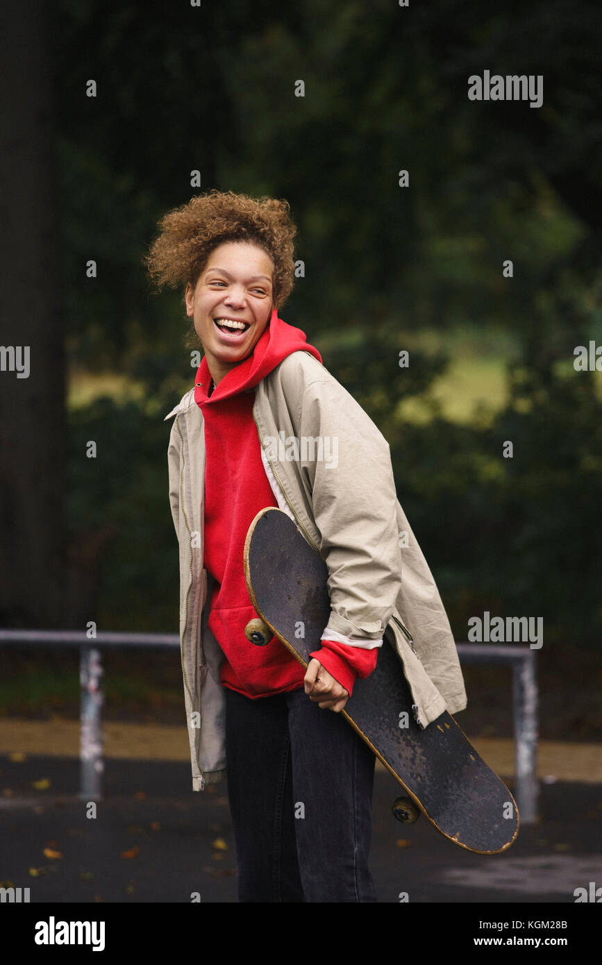 Cheerful woman carrying skateboard while standing at park Banque D'Images