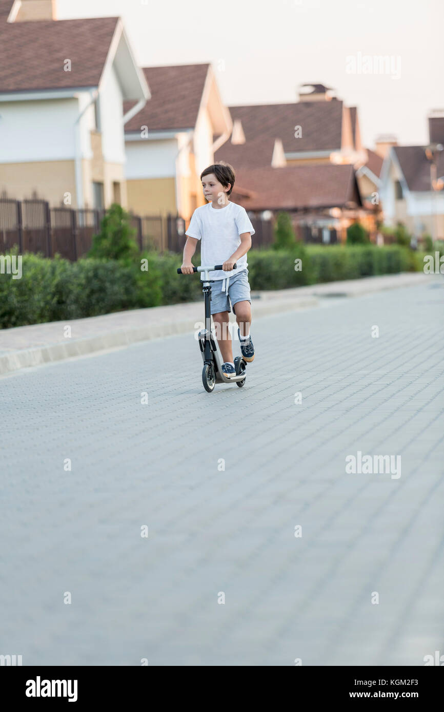 Boy riding scooter push sur la rue pavée de la ville Banque D'Images