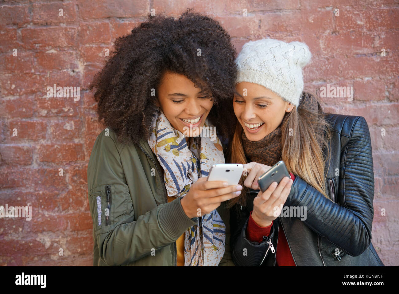 Trendy girls standing par mur jouant avec smartphone Banque D'Images