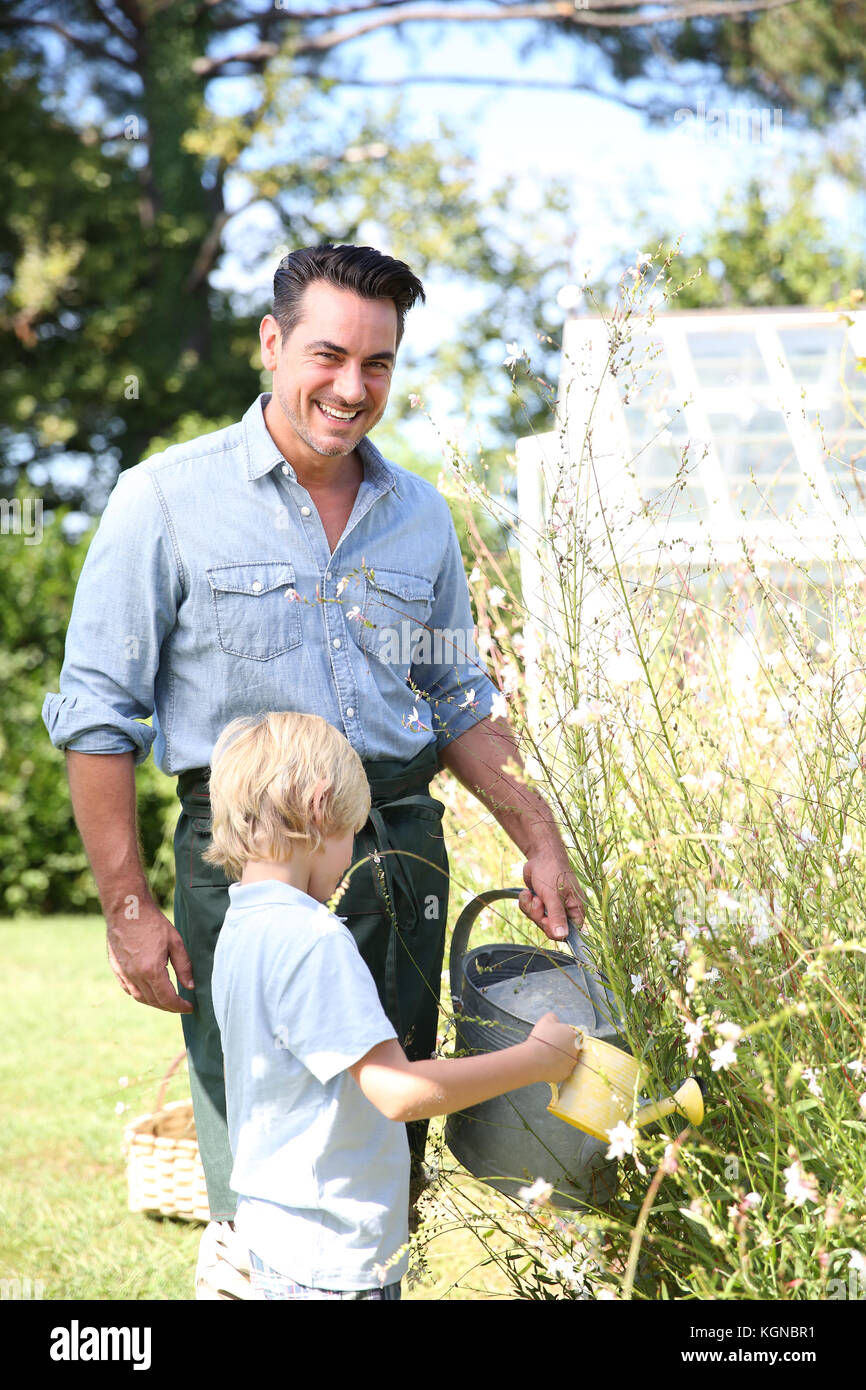 Père et fils watering plants in garden Banque D'Images