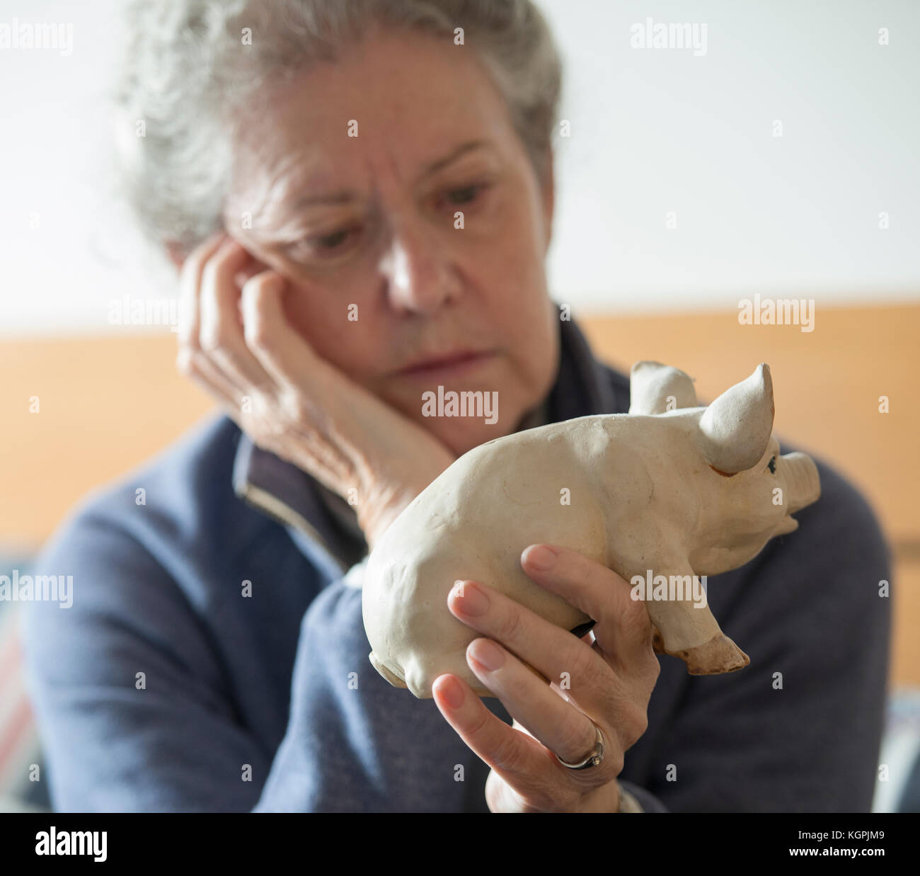 Femme plus âgée avec économiseur d'argent tirelire, à fond, avec tête appuyée sur la main, compte d'épargne taux d'intérêt restent bas, 2017. Banque D'Images
