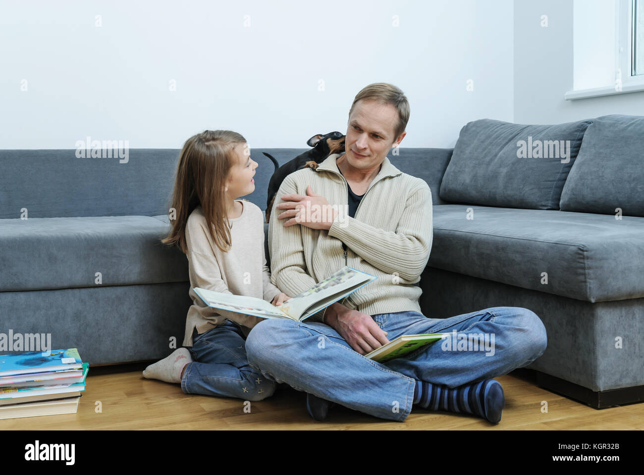 Père et fille sont la lecture de livres. le chiot est de jouer sur la table. Banque D'Images