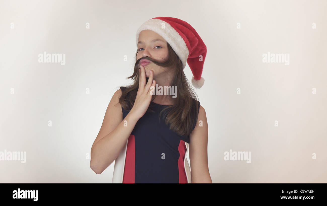 Beautiful happy girl adolescent dans un santa claus hat émotionnellement fools autour et fait une moustache hors de ses cheveux sur fond blanc Banque D'Images