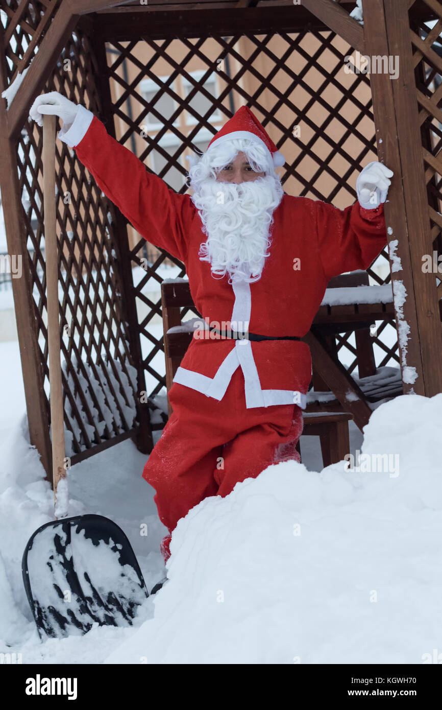 Le Père noël est fier de s'appuyer sur une pelle après avoir travaillé de la neige dépose devant la maison en bois Banque D'Images