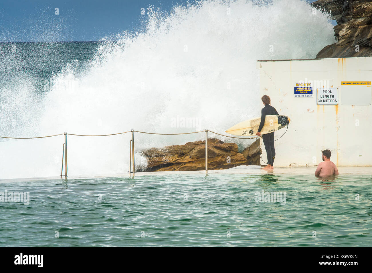 Un surfeur homme attend le bon moment pour entrer dans l'eau de la piscine de roche Bronte Beach à Sydney, NSW, Australie en grande surf Banque D'Images