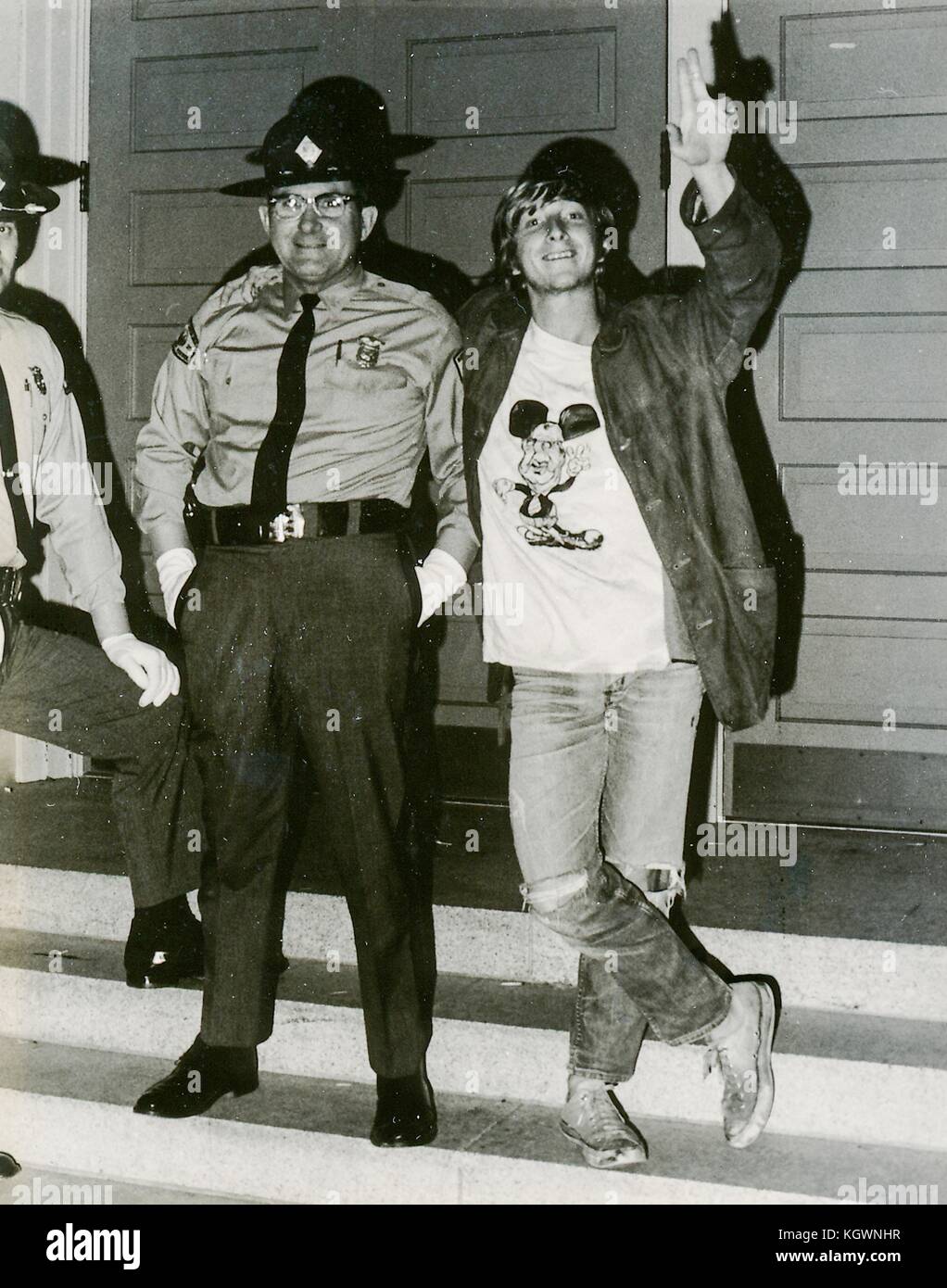 En étudiant une tenue hippie, y compris un t-shirt avec une caricature de l'homme politique représentant agnew Spiro Agnew dans le personnage Mickey Mouse, posant avec son bras autour d'un adjoint du shérif sur les marches d'un bâtiment lors d'une guerre du vietnam élève sit-in de protestation à la North Carolina State University, Raleigh, Caroline du Nord, 1970. Banque D'Images