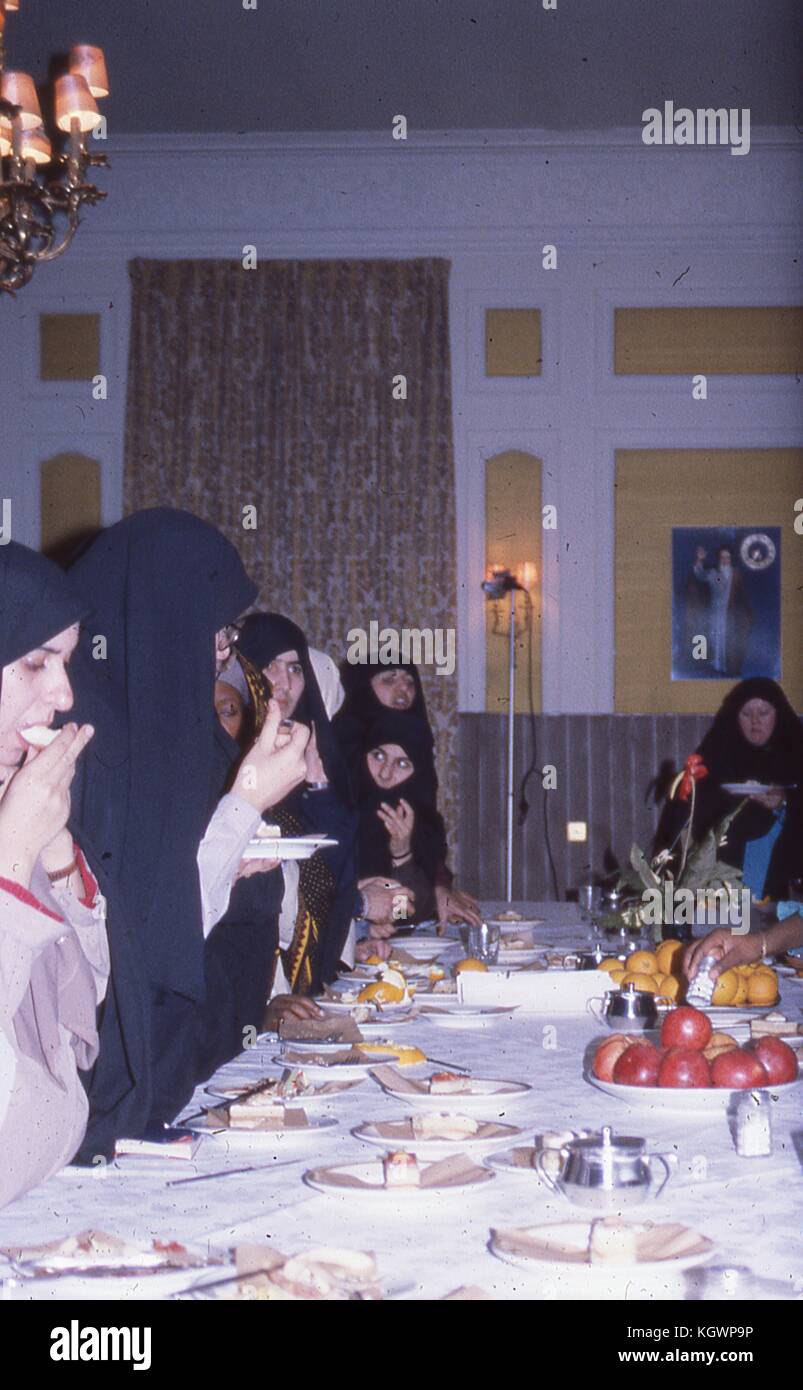 Scène d'un groupe de femmes musulmanes de différentes origines ethniques portant tchador, manger un gâteau et des fruits d'une longue table de banquet dans un hôtel en Iran, mars, 1983. D'importants dégâts sur l'original. () Banque D'Images
