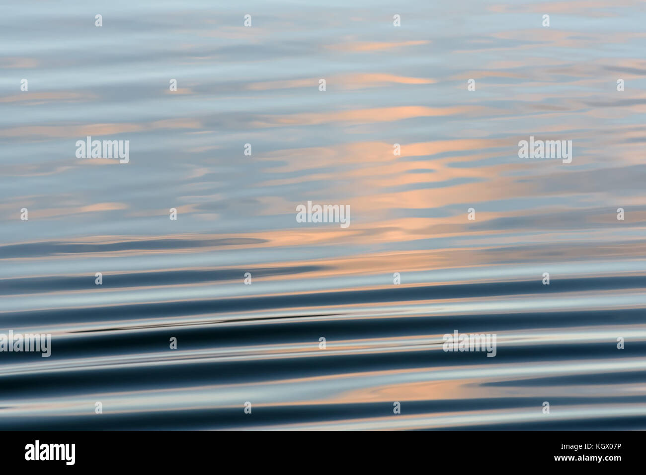 Abstract natural background avec des reflets de ciel et de nuages et une belle vagues sur l'eau bleue du lac au coucher du soleil Banque D'Images