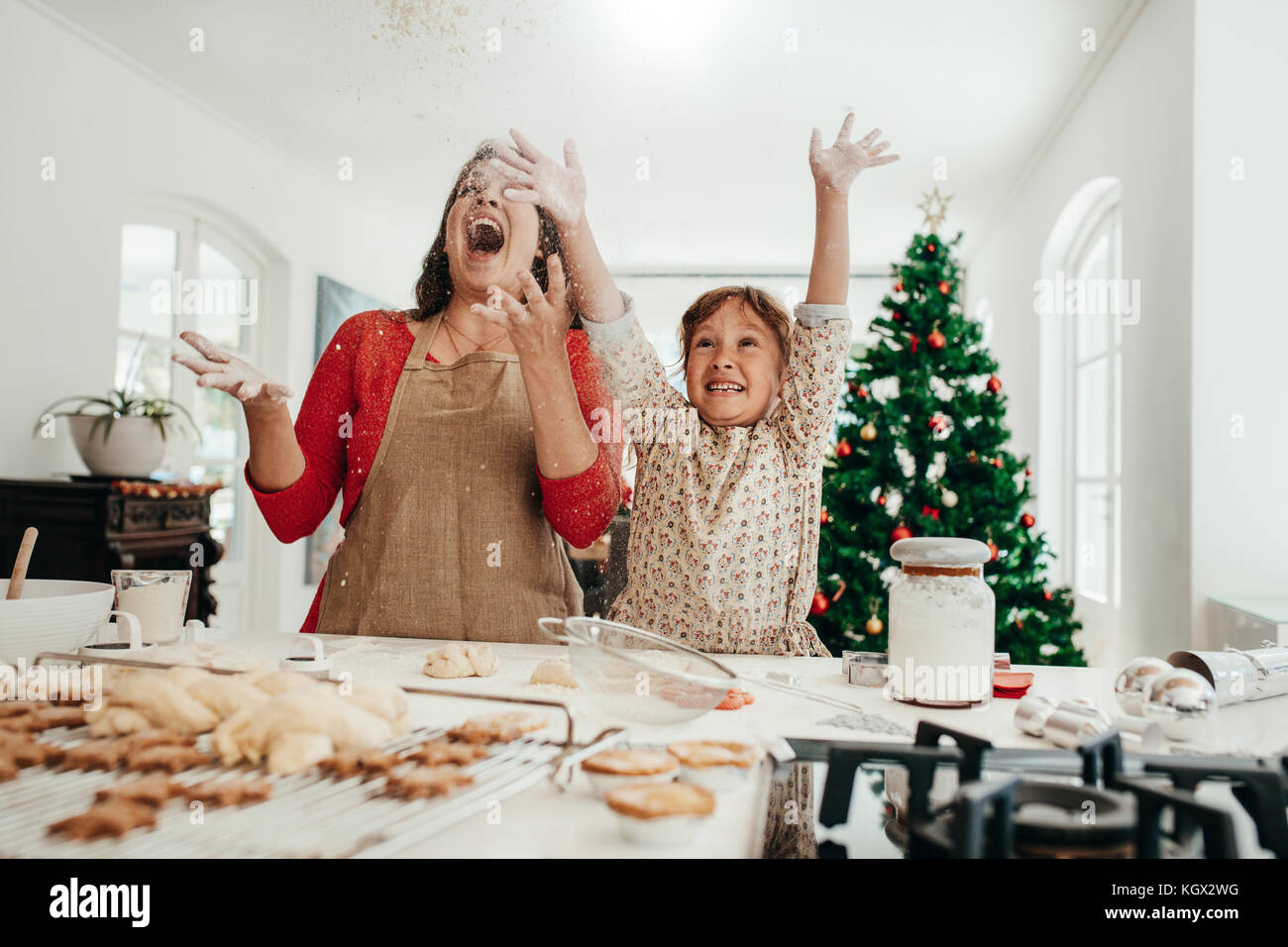 Heureuse mère et fille dans la cuisine jeter la farine dans l'air tout en faisant des cookies. Star boulangerie cookies, muffins et d'épices sur une table de cuisine avec déc Banque D'Images