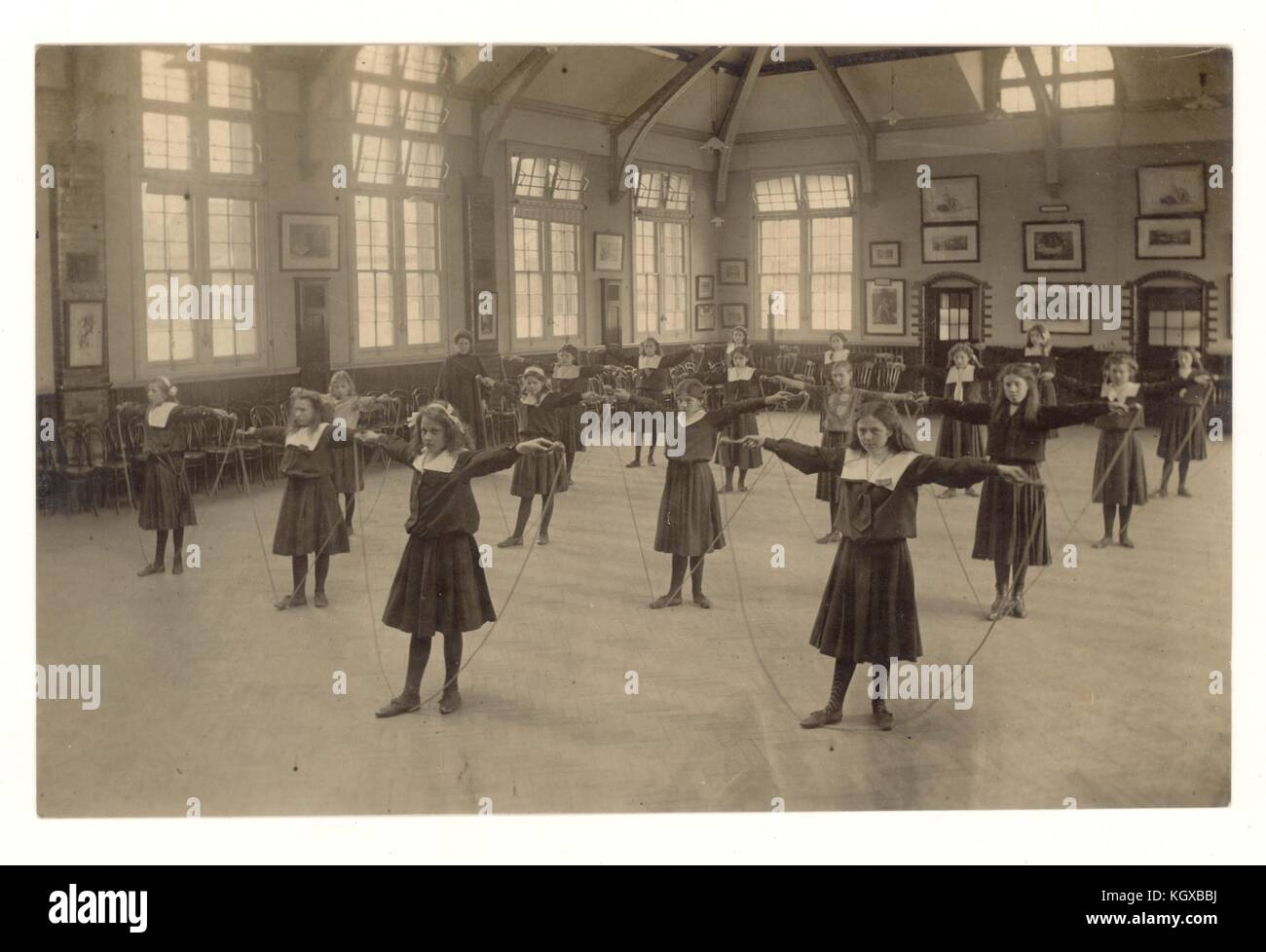 Début des années 1900, carte postale édouardienne de P.E. class - filles sautant en salle d'école, U.K. Edwardians Banque D'Images