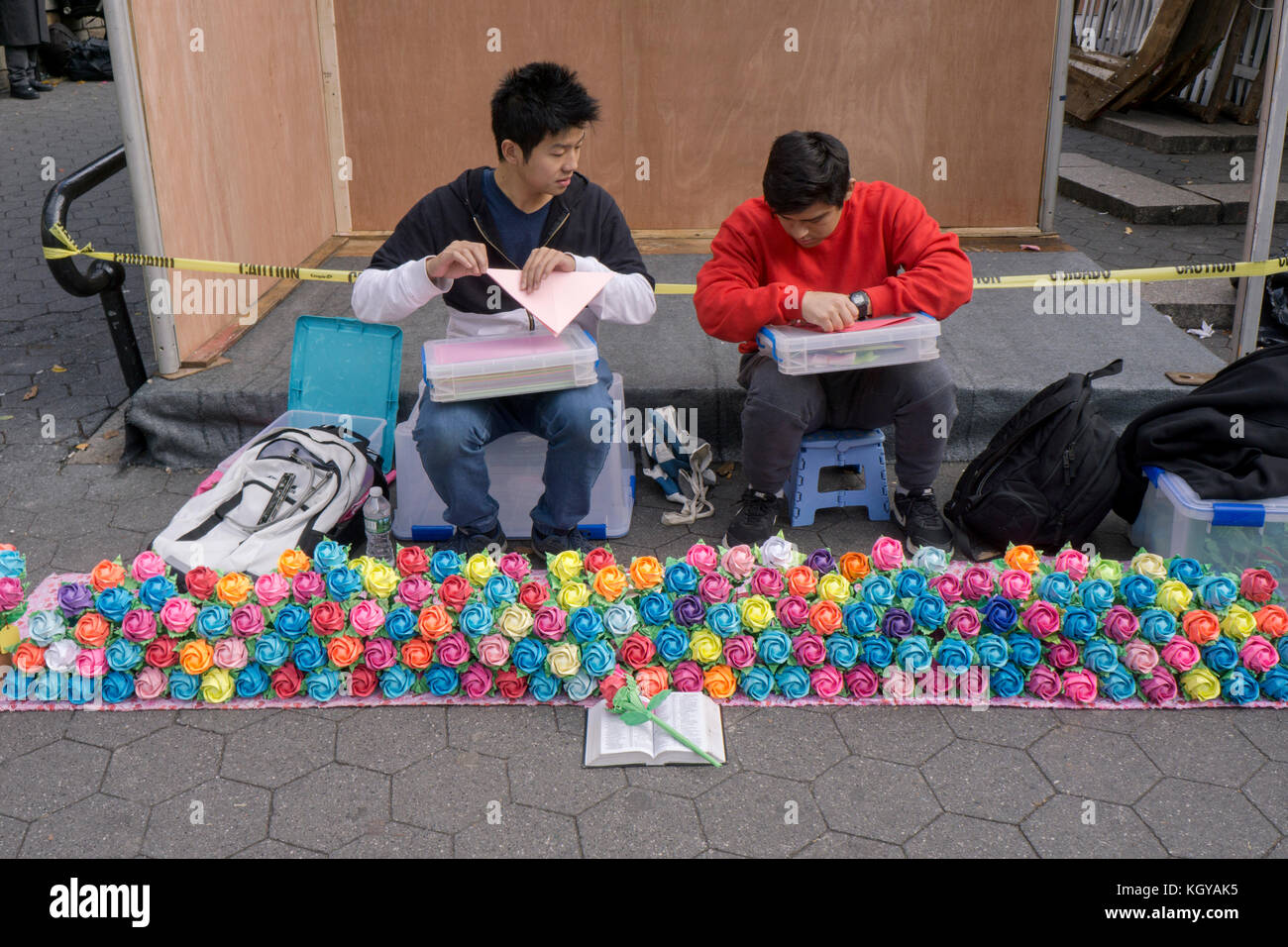 Un jeune homme américain chinois coloré fleurs origami fait et indique à son ami dans l'origami. À Union Square Park à Manhattan, New York City Banque D'Images
