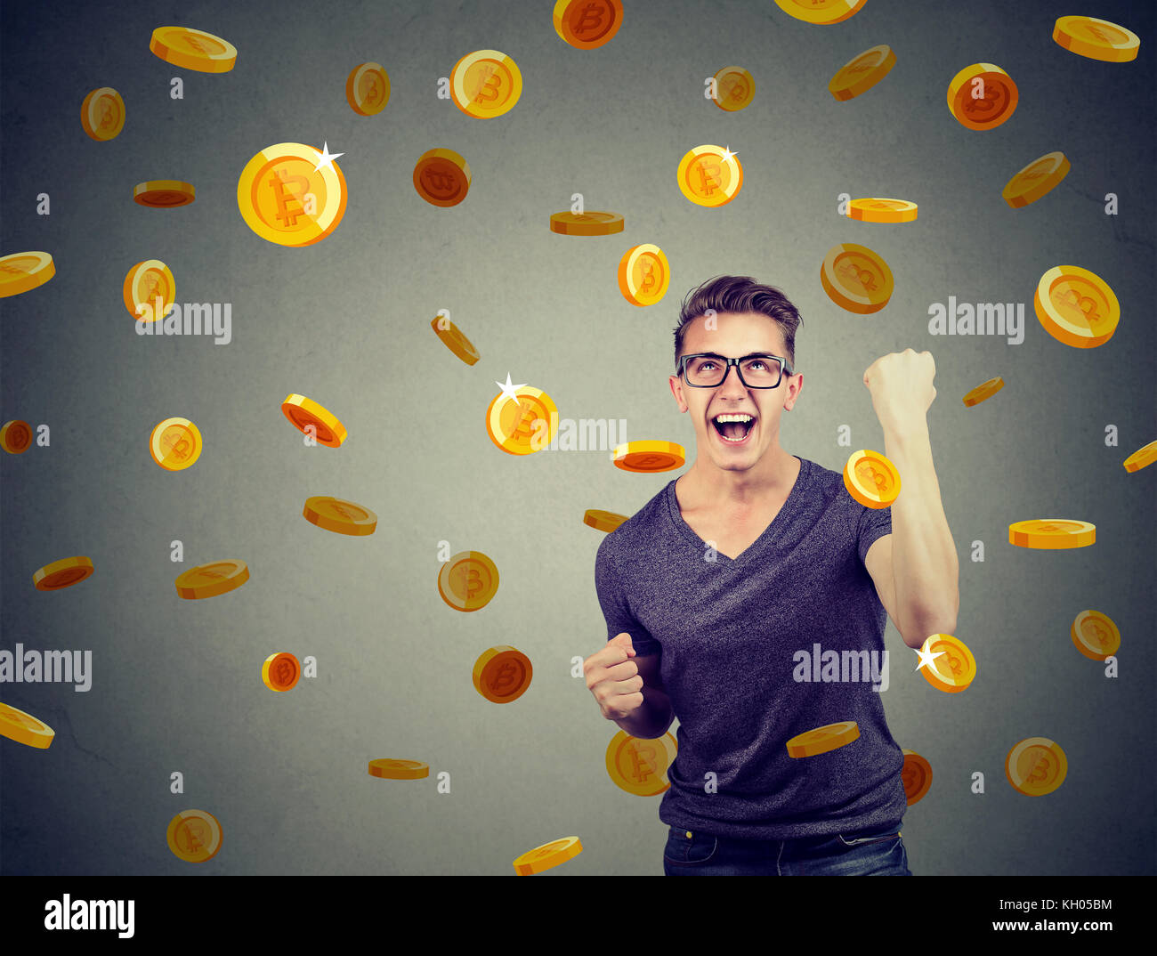 Portrait d'un jeune homme heureux de célébrer la réussite financière sous une pluie bitcoin sur un fond de mur gris. Banque D'Images