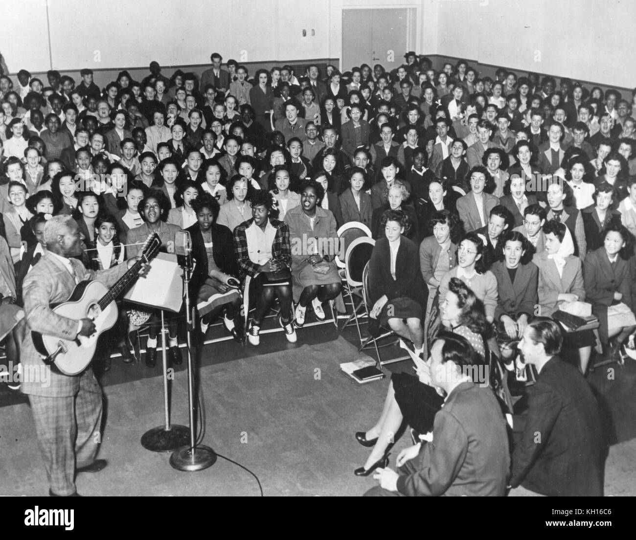 Huddie William Ledbetter (1888-1949), un musicien de blues et folk plus connu sous le nom de 'Leadbelly,' exécute devant un auditoire de jeunes d'âge scolaire, s'accompagnant sur sa guitare à 12 cordes, San Francisco, CA, 1949. Banque D'Images