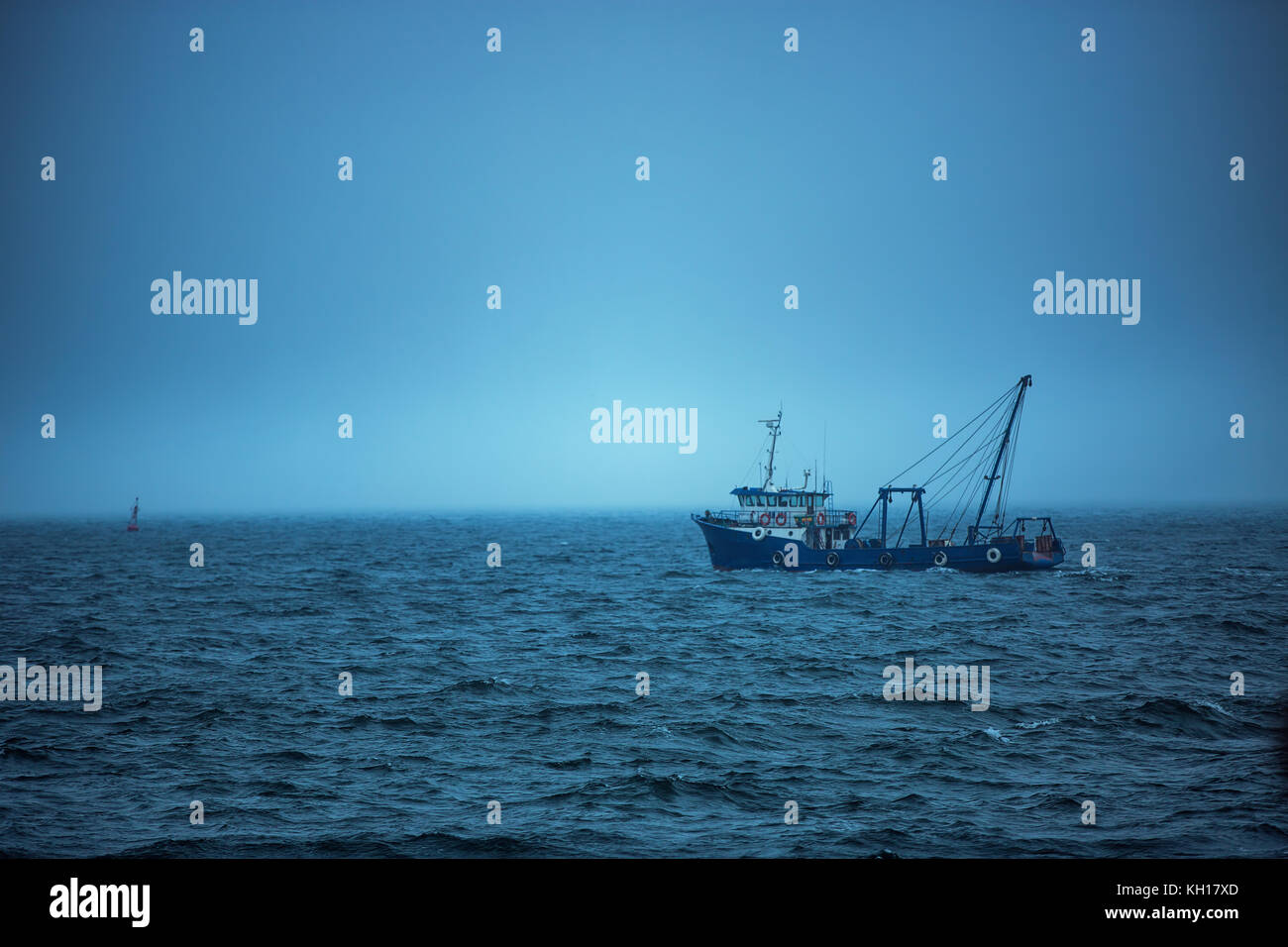 Bateau de pêche chalutier naviguant dans les eaux ouvertes sur un matin brumeux et froid, sunrise Banque D'Images