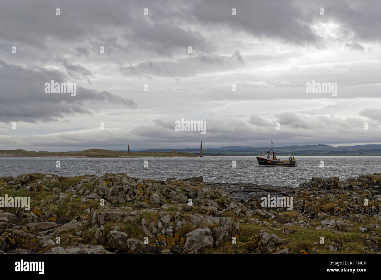 Bateau de pêche Shell Britannia II en activité au large de l'île à l'Île Sainte de ruse avec l'ancien droit d'aides à la navigation dans l'arrière-plan Banque D'Images