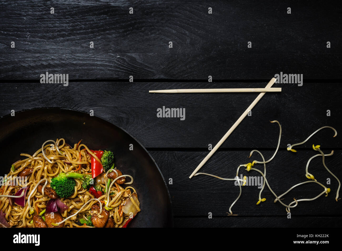 Udon nouilles sauté au poulet et légumes au wok casserole sur fond de bois noir. avec des baguettes. vue d'en haut. Banque D'Images