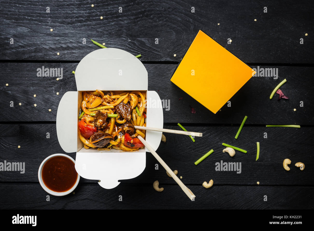 Udon nouilles sautés avec de la viande et des légumes dans une boîte sur fond noir. avec des baguettes et de la sauce. vue d'en haut. Banque D'Images