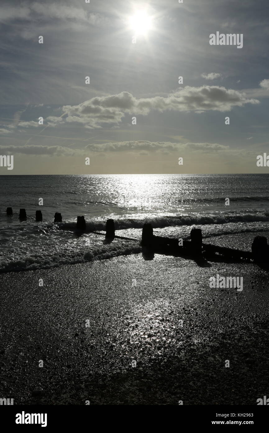 Bognor Regis. Le soleil se reflète au large de la mer sur une plage déserte de la côte sud du Royaume-Uni. Mer calme, marée basse. Montre des brise-lames en bois pour empêcher l'érosion côtière. Banque D'Images