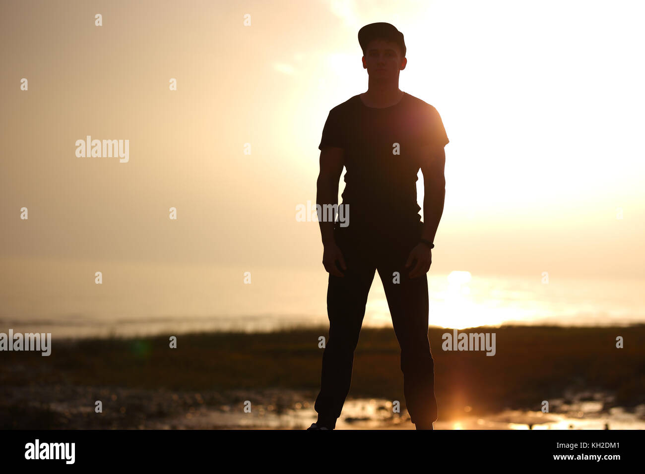 Silhouette of man standing on beach dans le coucher du soleil sur la mer. Banque D'Images Silhouette of man standing on beach dans le coucher du soleil sur la mer. Banque D'Images