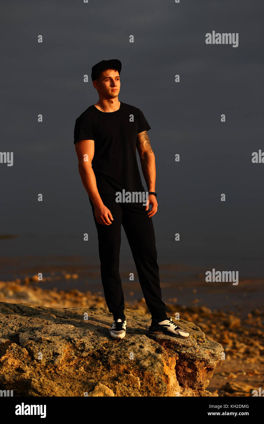 Homme debout sur la plage rocheuse dans le coucher du soleil sur la mer. Banque D'Images Homme debout sur la plage rocheuse dans le coucher du soleil sur la mer. Banque D'Images