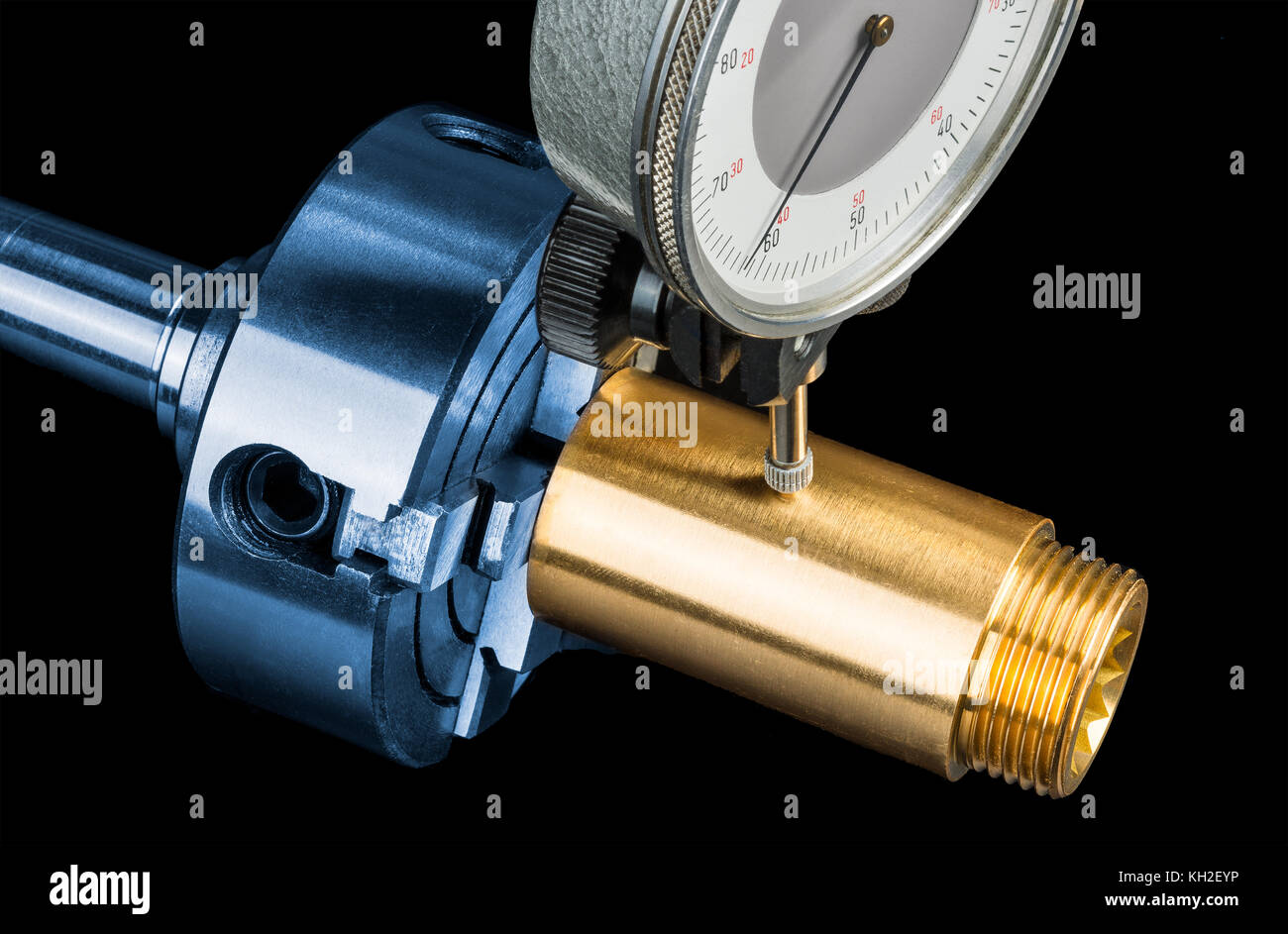 La mesure de la tolérance dans la pièce en laiton raccord d'or. Chuck dans la mâchoire de serrage et l'indicateur à cadran sur fond noir. L'ingénierie, l'éducation, de l'industrie. Banque D'Images