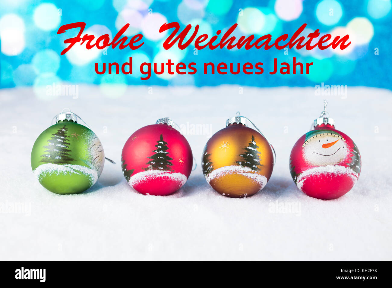 Groupe de boules de Noël colorées avec du texte en allemand "frohe weihnachten und gutes neues jahr' dans la neige blanche. Banque D'Images