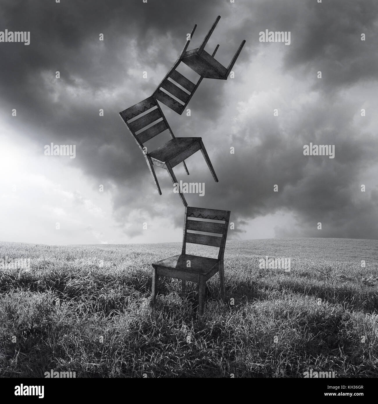 Une image surréaliste représentant trois chaises déménagement vol isolé dans une prairie avec une forte et ciel nuageux en noir et blanc Banque D'Images