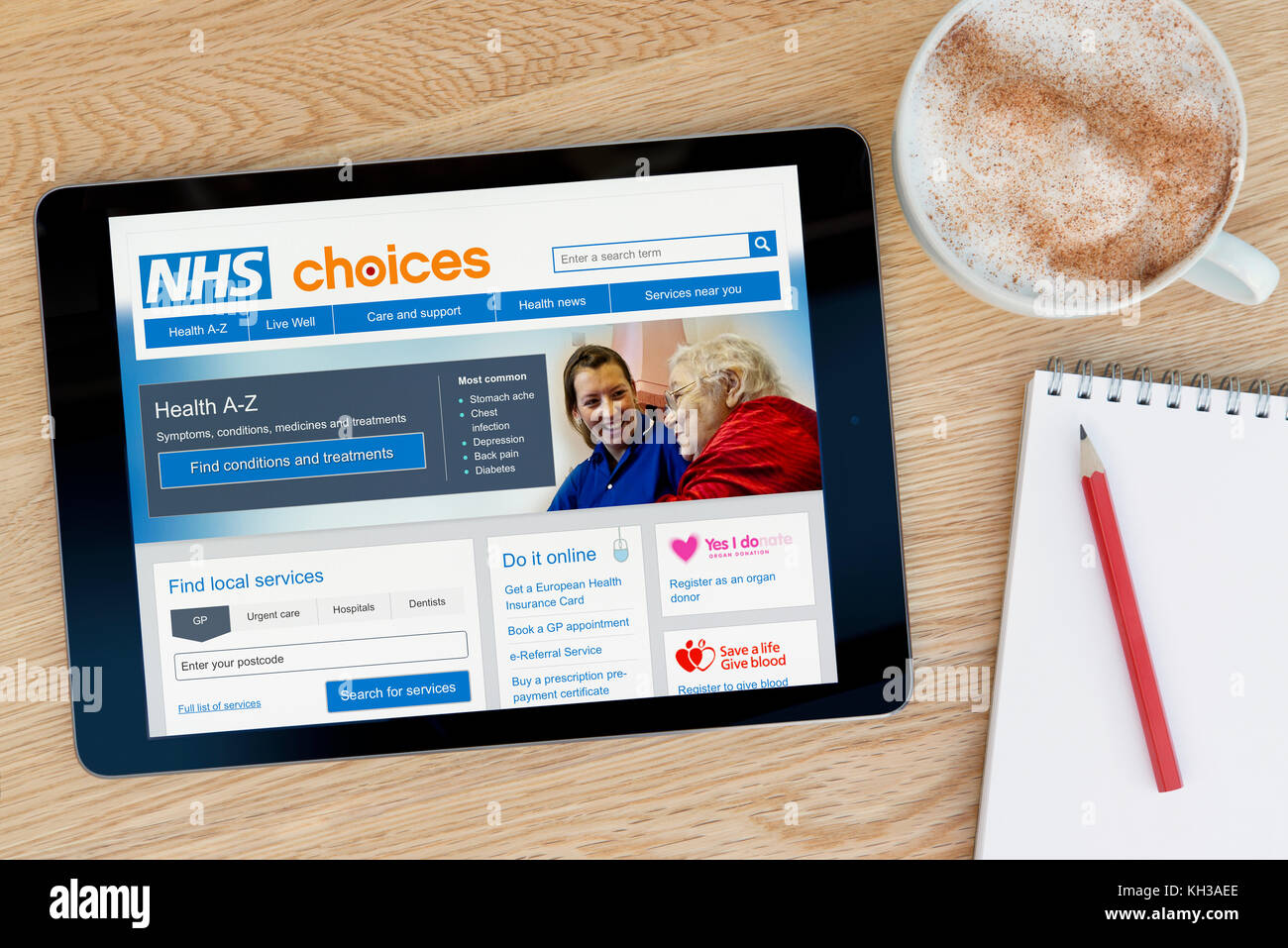 Le site web présente des choix du NHS sur un iPad tablet device qui repose sur une table en bois à côté d'un bloc-notes et un crayon et une tasse de café (rédaction) Banque D'Images