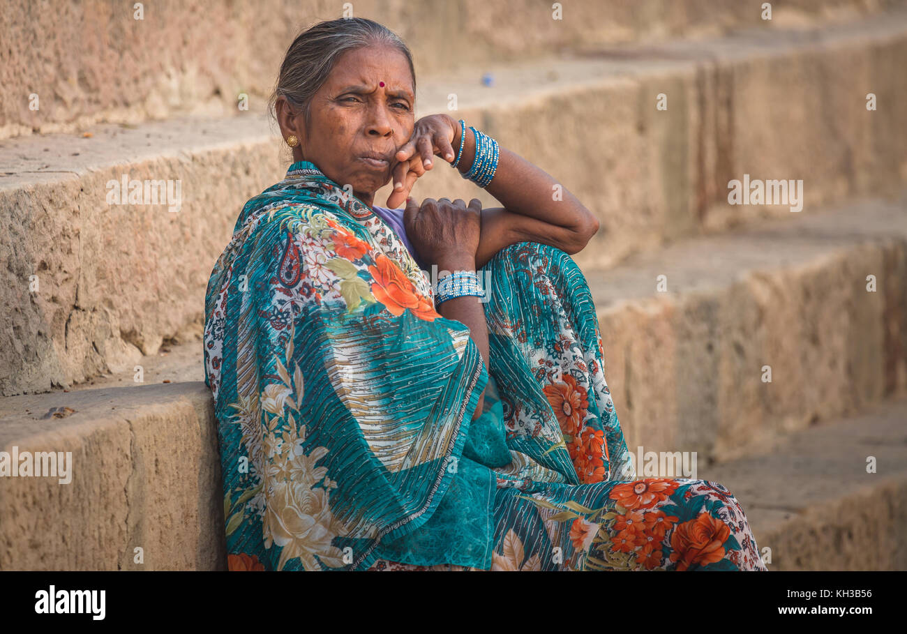 Femme d'âge indien avec un air pensif assis sur l'escalier du Gange ghat à Varanasi, Inde. Banque D'Images