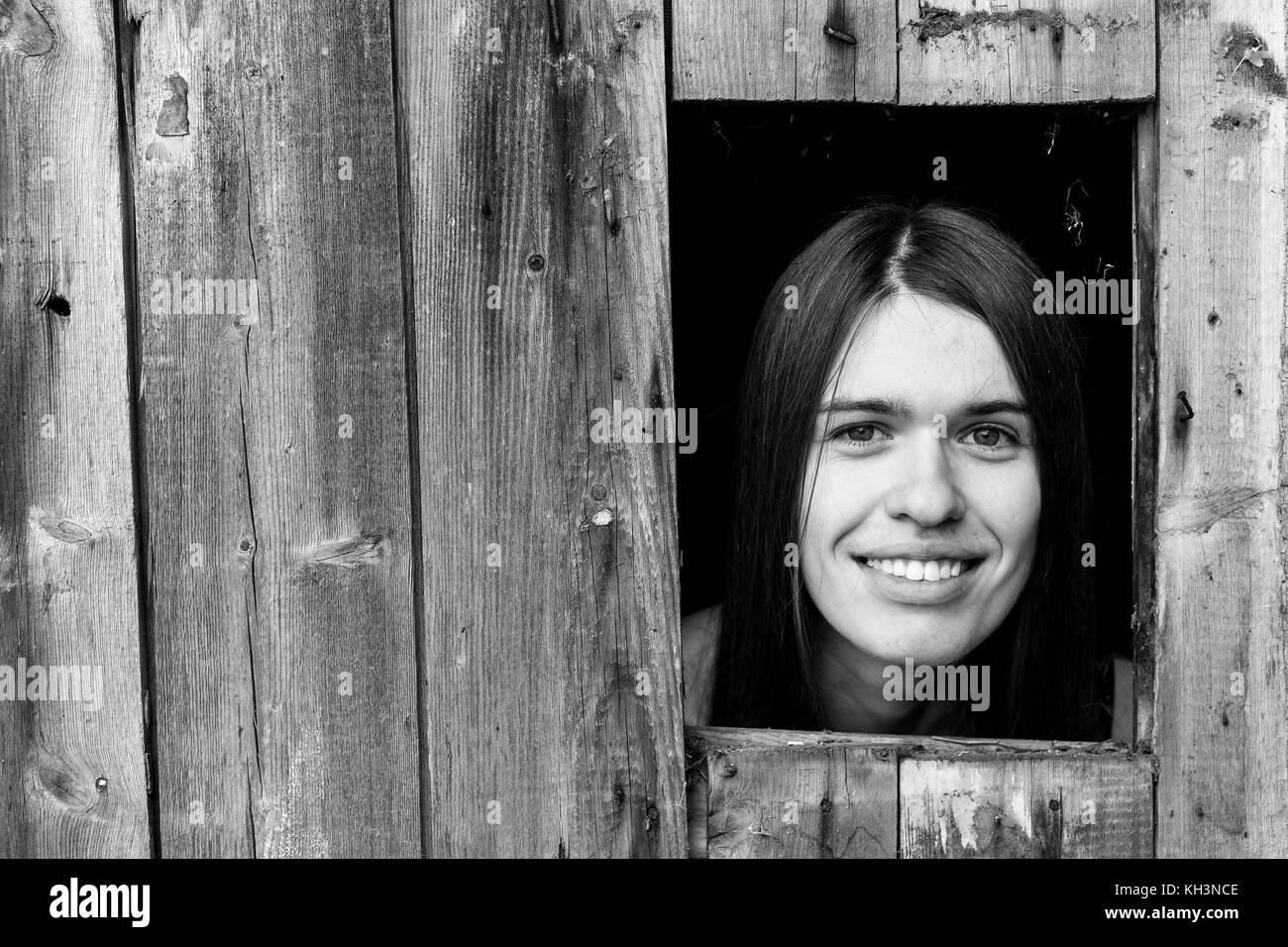 Une jeune femme enfermée dans une cabane en bois, peeking through une petite fenêtre. noir et blanc photo. Banque D'Images