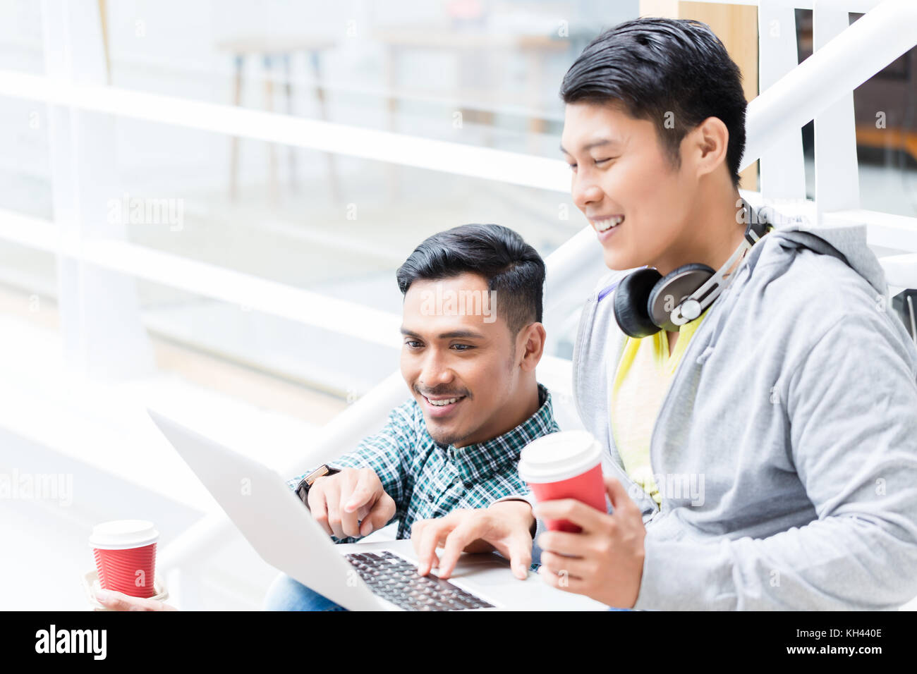 Deux jeunes hommes asiatiques en utilisant un ordinateur portable tout en vous relaxant pendant les pauses Banque D'Images