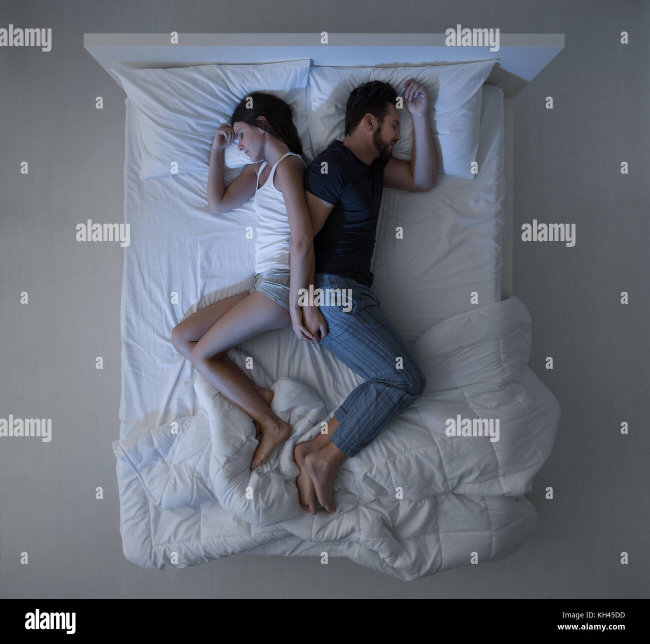 Jeune couple aimant dormir dans le lit dos à dos et tenir la main, vue du dessus Banque D'Images