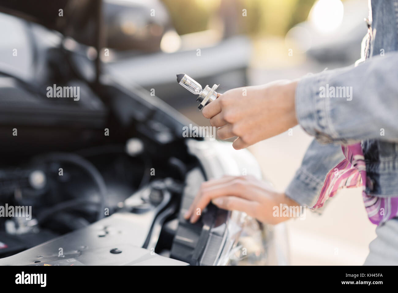 Femme du remplacement d'une ampoule de phare cassé dans sa voiture, elle est tenue d'une nouvelle ampoule et s'appuyant sur la voiture avec capot Banque D'Images