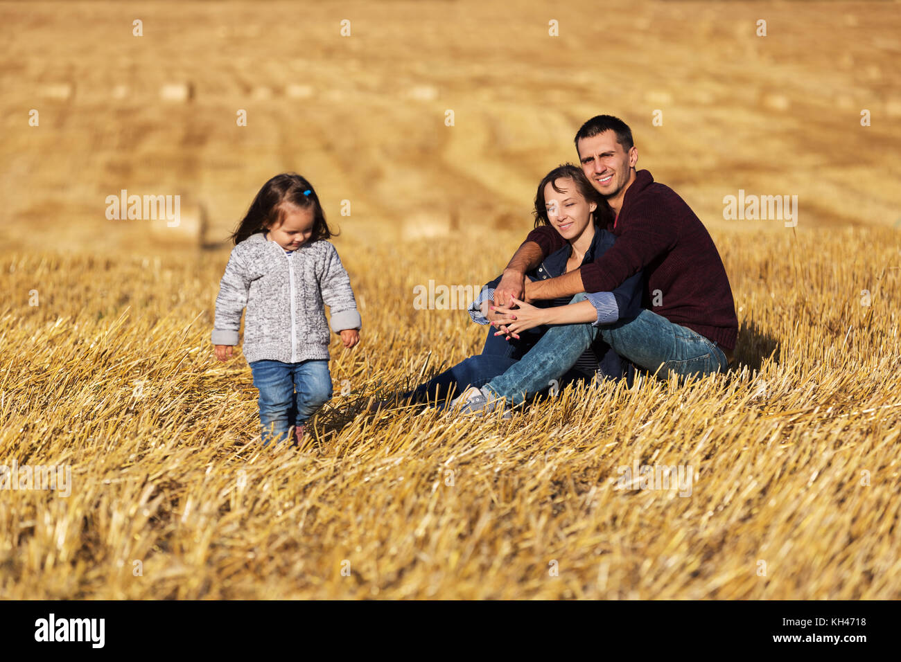 Heureux jeune famille avec 2 ans, assis sur le sol dans le champ moissonné Banque D'Images