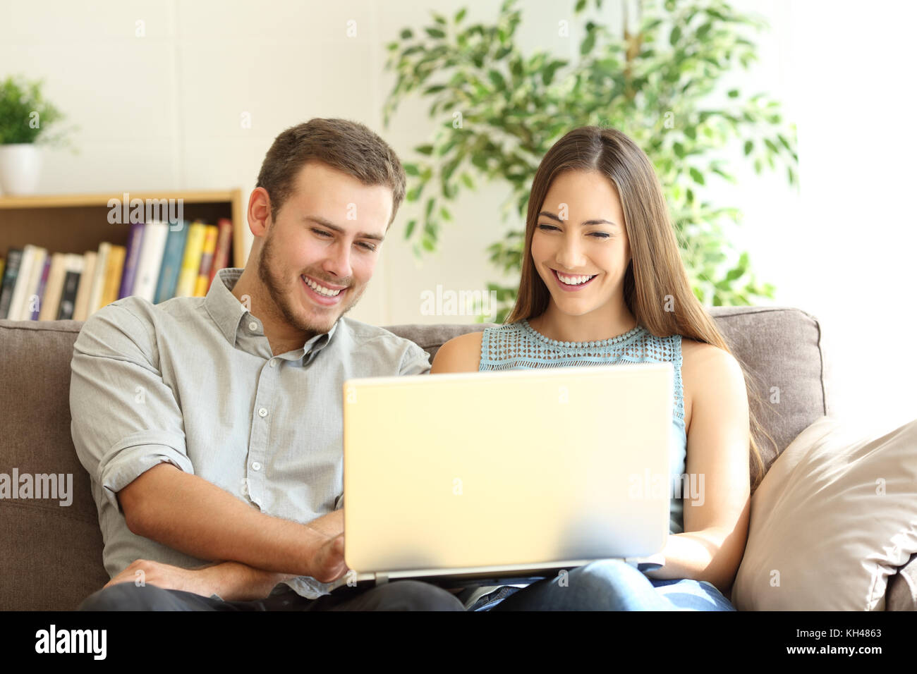 Vue avant, portrait d'un jeune couple heureux à l'aide d'un laptop assis sur un canapé dans la salle de séjour à la maison Banque D'Images