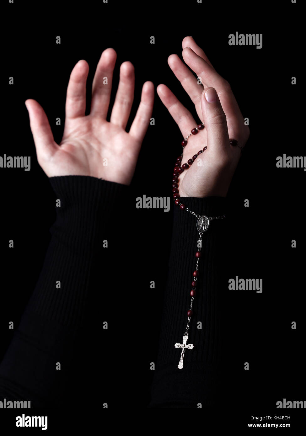 Les mains avec les bras tendus priant et holding chapelet avec croix ou crucifix. fond noir. femme avec la foi chrétienne catholique Banque D'Images