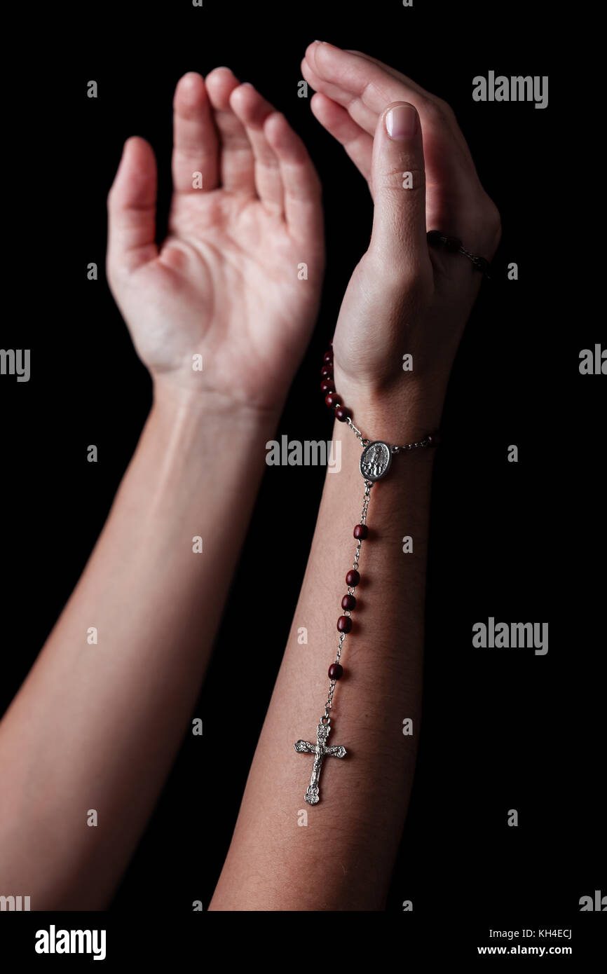Les mains avec les bras tendus priant et holding chapelet avec croix ou crucifix. fond noir. femme avec la foi chrétienne catholique Banque D'Images