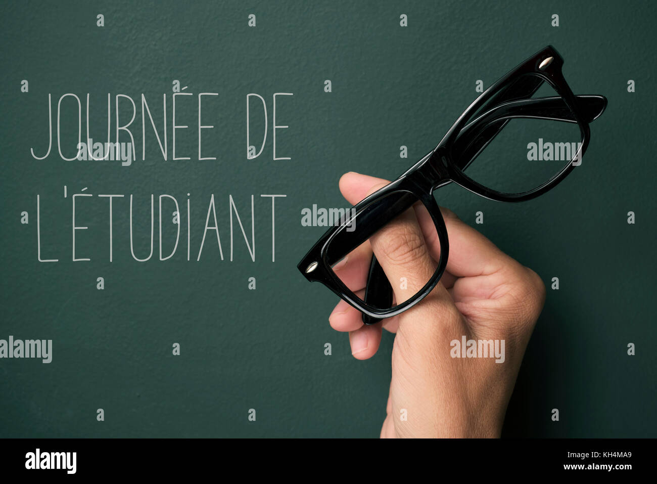 Une paire de lunettes cerclées de noir en plastique dans la main d'un jeune homme et le texte journee del etudiant, la journée des élèves en français, contre une chalkb vert Banque D'Images