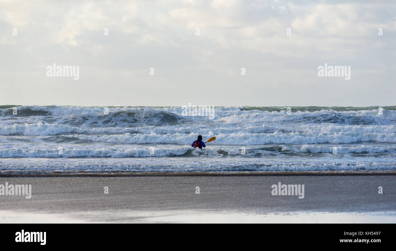 Un solitaire pagaie de kayak en mer à travers les vagues comme ils rouler jusqu'à la plage de Polzeath, North Cornwall, UK sur une journée ensoleillée d'automne. Banque D'Images