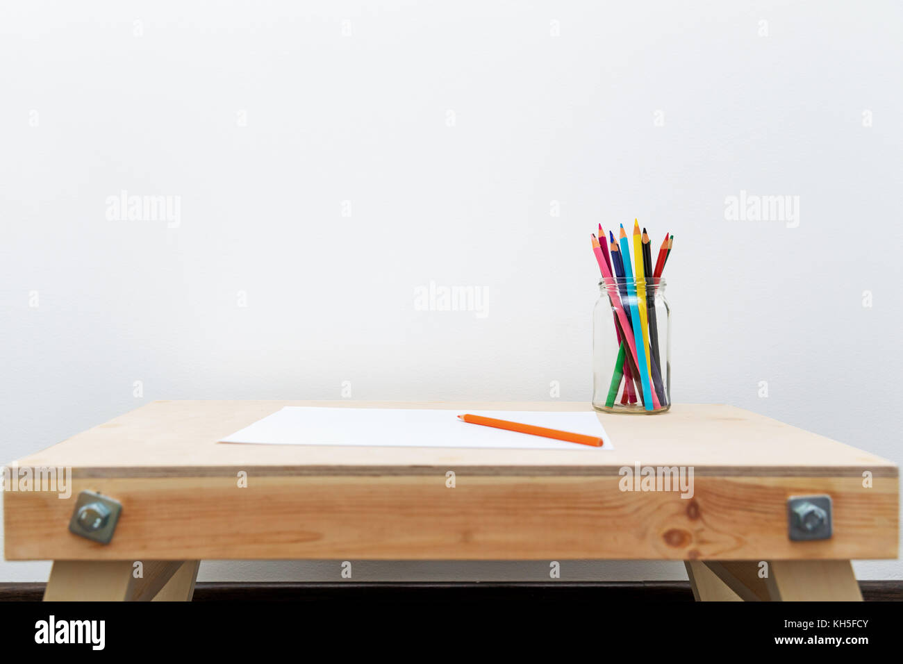 Enfant en bois table de dessin avec des crayons de couleurs par le mur blanc Banque D'Images