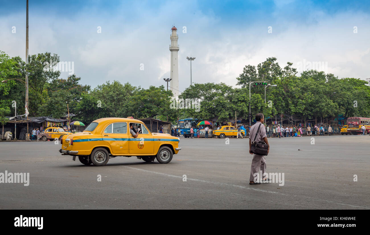 L'homme tout en traversant une route un taxi jaune passe à côté à l'dharamtala ville intersection donnant sur le célèbre monument ochterlony à Kolkata. Banque D'Images