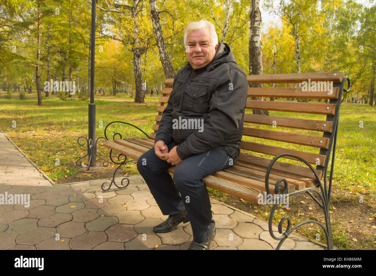 Seul le vieil homme aux cheveux gris, reposant sur un banc en bois dans un parc sur une journée ensoleillée d'automne. Banque D'Images