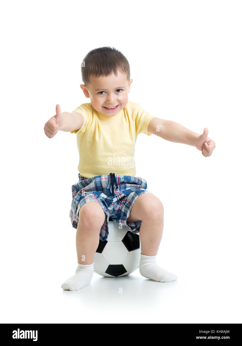 Enfant garçon est assis sur un ballon de soccer avec Thumbs up sign. Banque D'Images