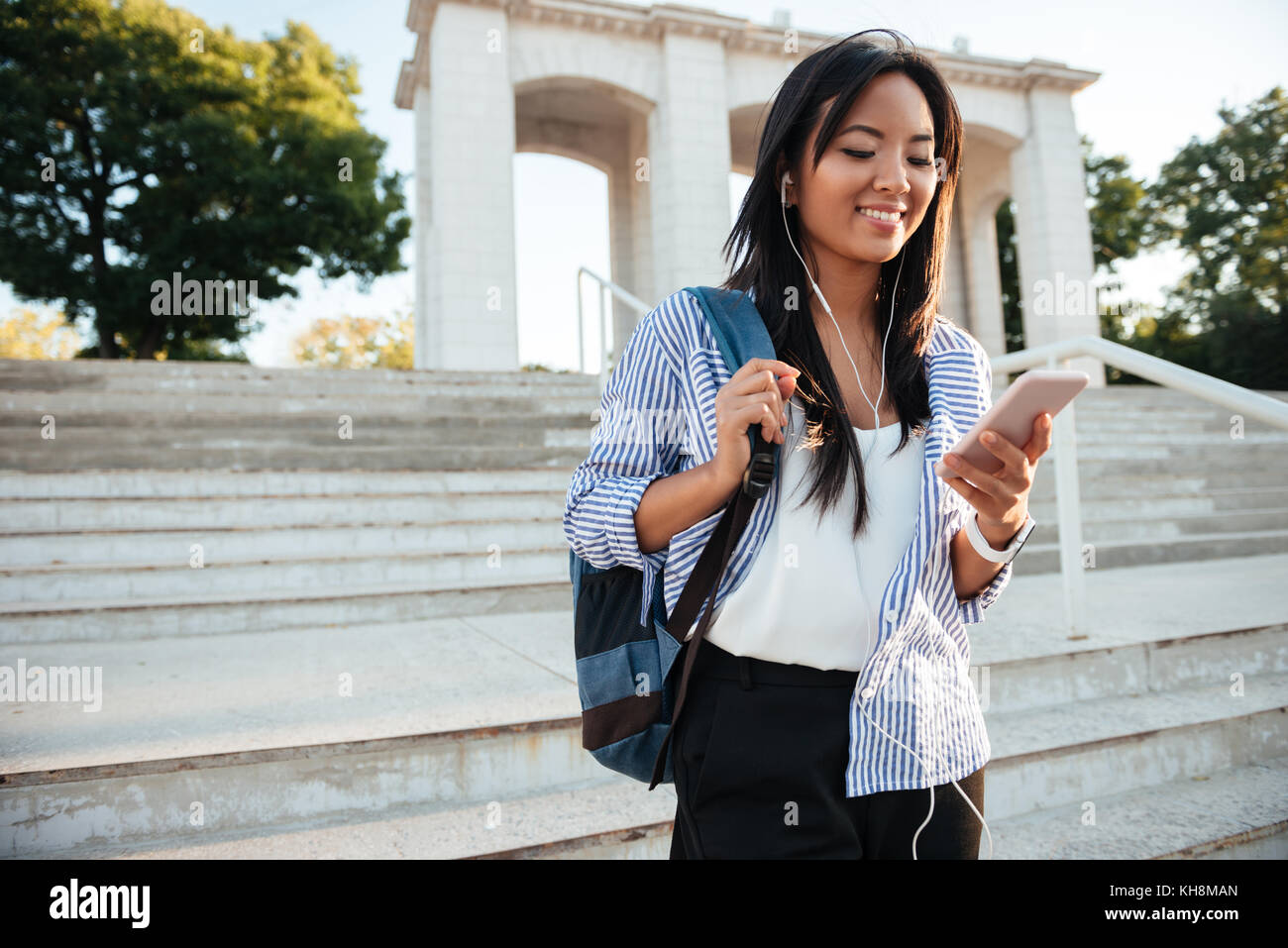 Young Asian woman en chemise rayée contrôler son téléphone, en descendant les escaliers Banque D'Images