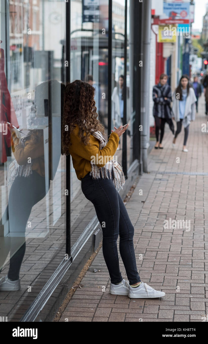 Adolescent utilisant un téléphone portable appuyé contre une vitrine Banque D'Images