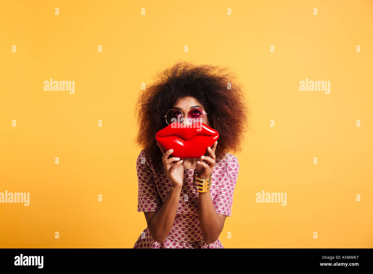 Assez élégant rétro femme africaine s'amuser tout en se posant avec de grandes lèvres rouge, à la recherche vers le haut, isolé sur fond jaune Banque D'Images